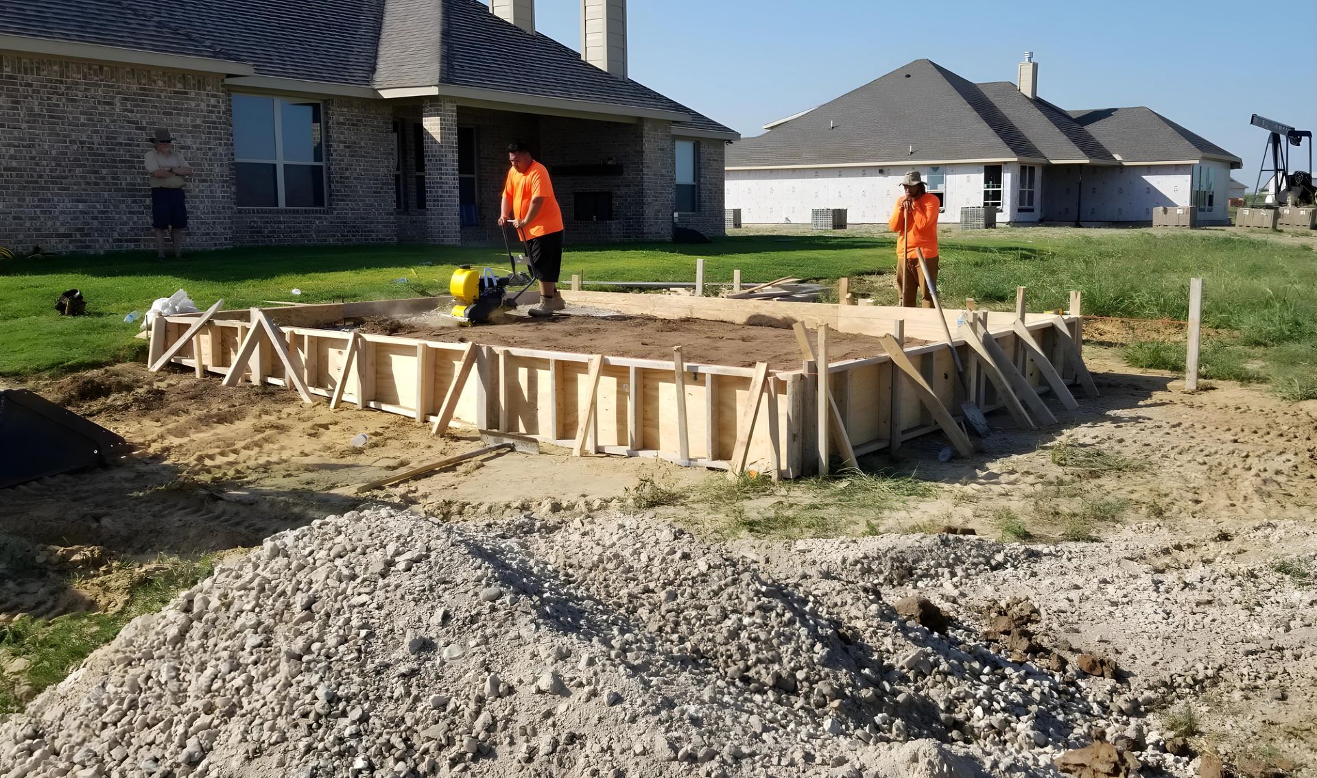 Two men are working on a concrete foundation in front of a house