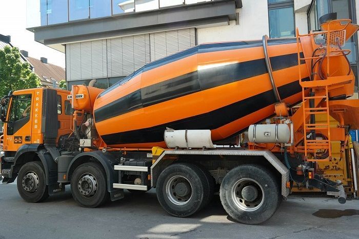 An orange and black concrete mixer truck is parked in front of a building