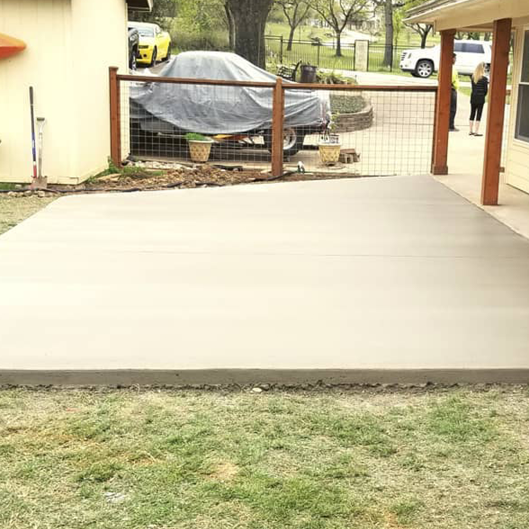 A concrete patio with a wooden fence and a car parked in the background.