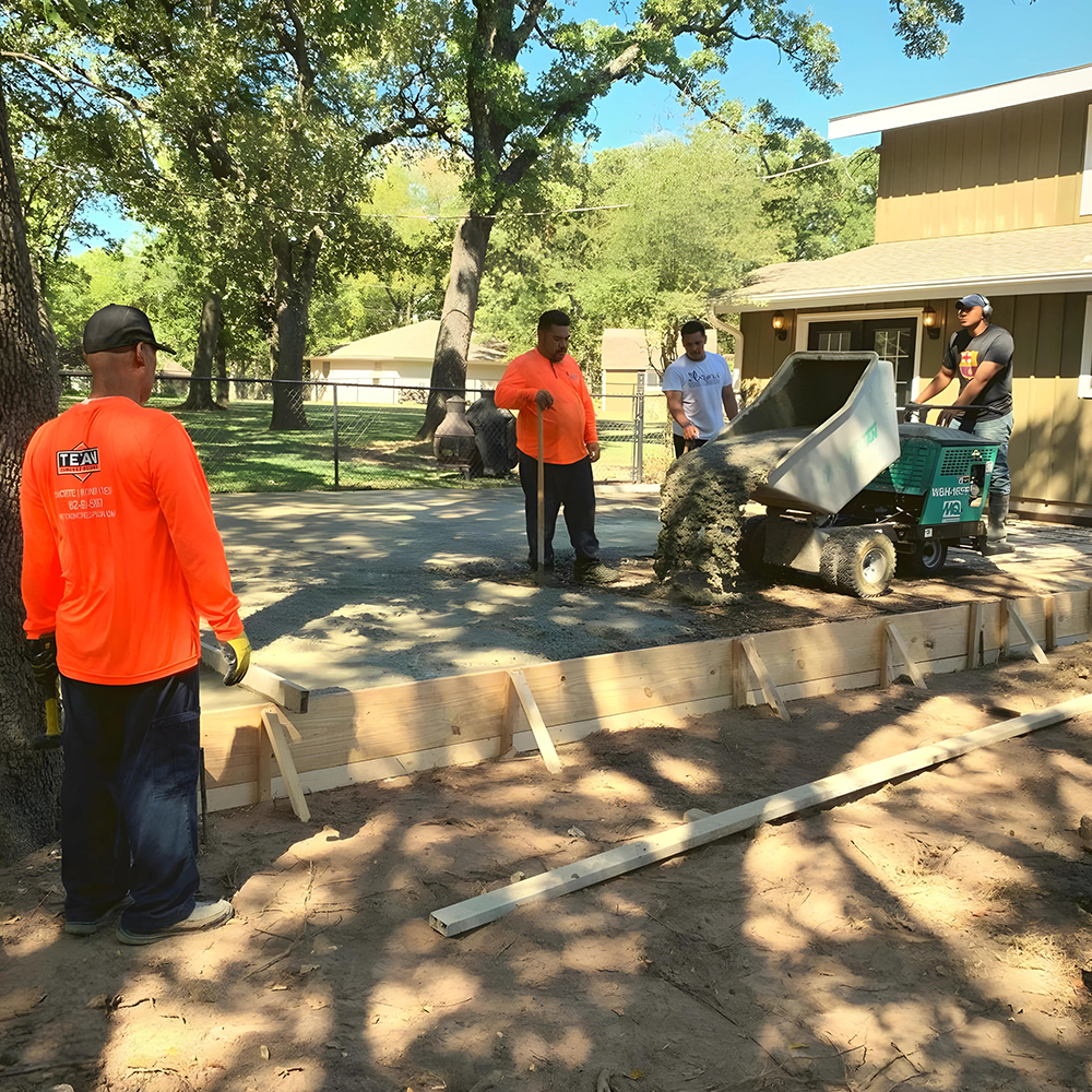 A concrete patio is being built in the backyard of a house.
