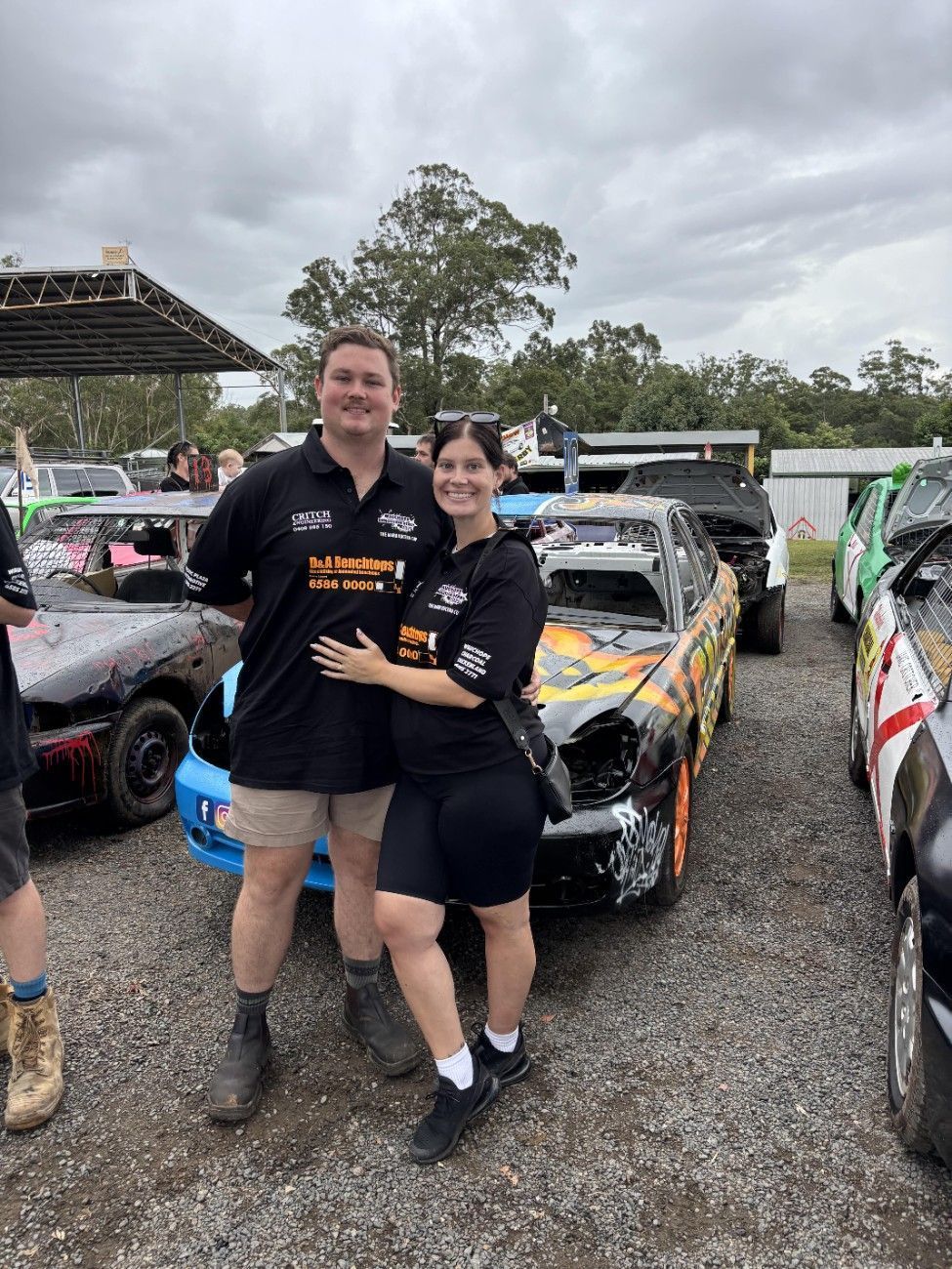 A man and a woman are posing for a picture in front of a race car — Pacific Plaza Automotive in Port Macquarie, NSW