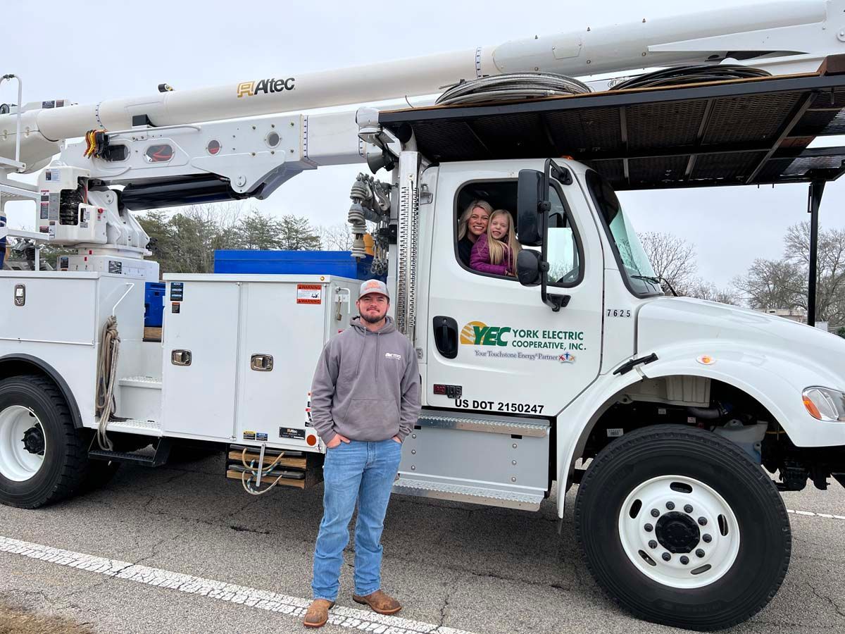 White utility bucket truck with a man standing beside it and a person in the cab on a cloudy day