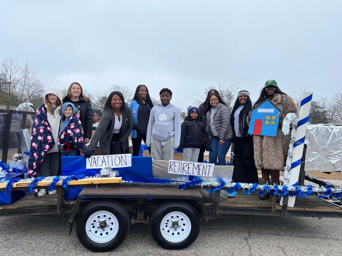People standing on a blue-and-white parade float with signs reading “Vacation” and “Friends”