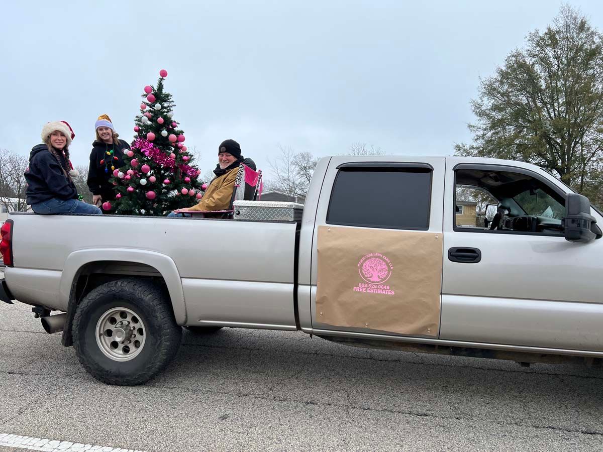 Decorated pickup truck with people and a Christmas tree riding in the truck bed.