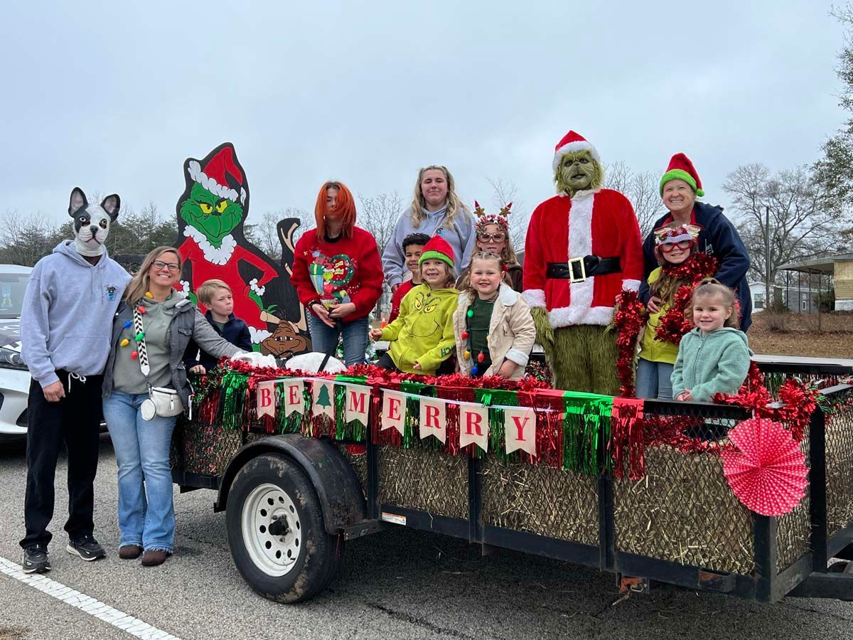 People in holiday costumes posing on a decorated trailer with a Merry Christmas banner.