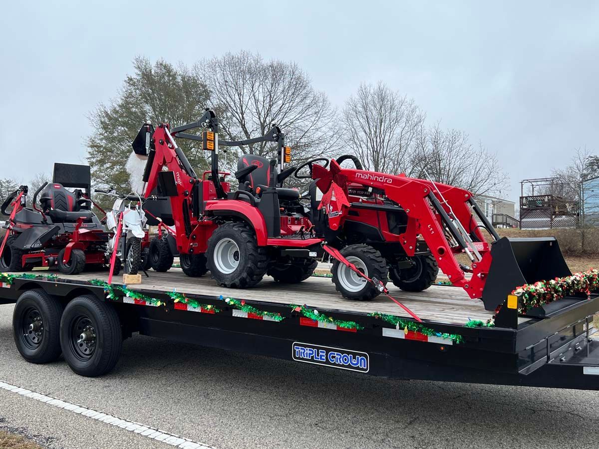 Red tractor loader on a black trailer parked outdoors under a cloudy sky