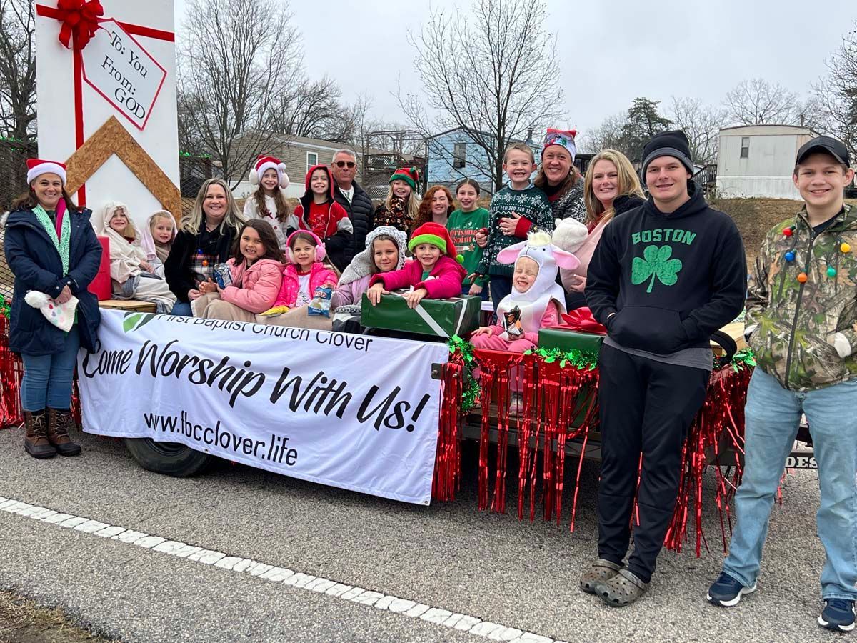 Group of people at a winter parade holding a “Love & Worship With Us!” banner and gifts