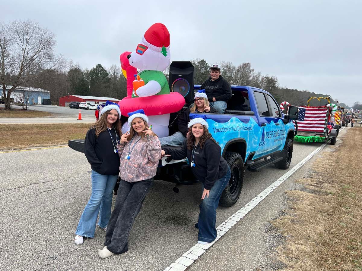 Three people pose beside a blue truck carrying a giant inflatable Santa on a parade route.