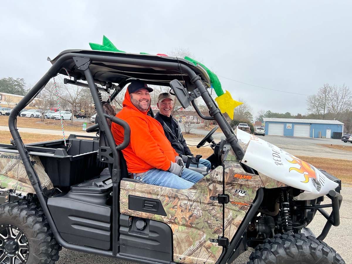 Two people in a camo UTV with green and yellow star balloons on an outdoor lot
