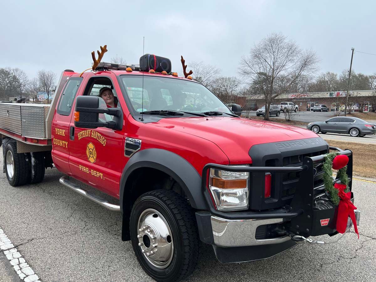 Red tow truck with holiday reindeer decorations parked in a lot under a cloudy sky
