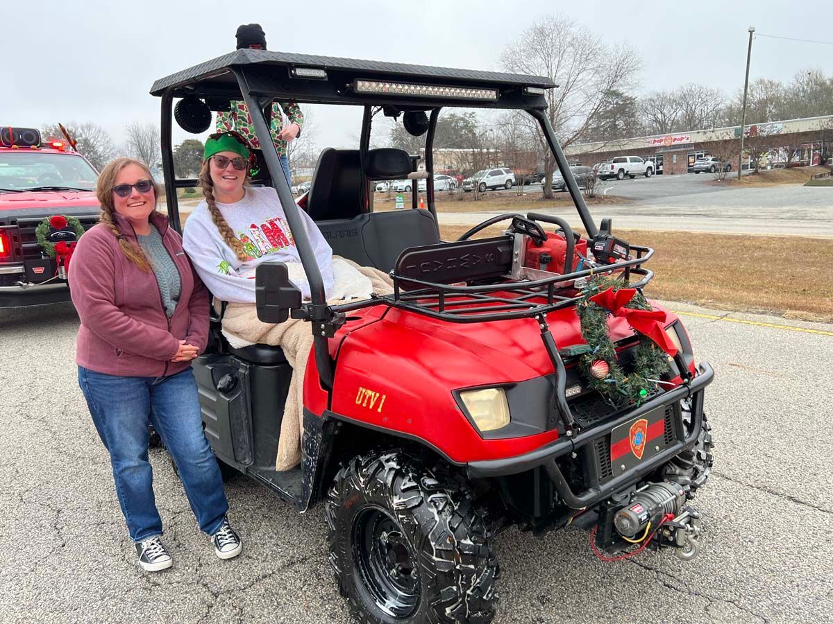 Two people posing beside a red utility ATV with holiday decorations on a roadside outdoors
