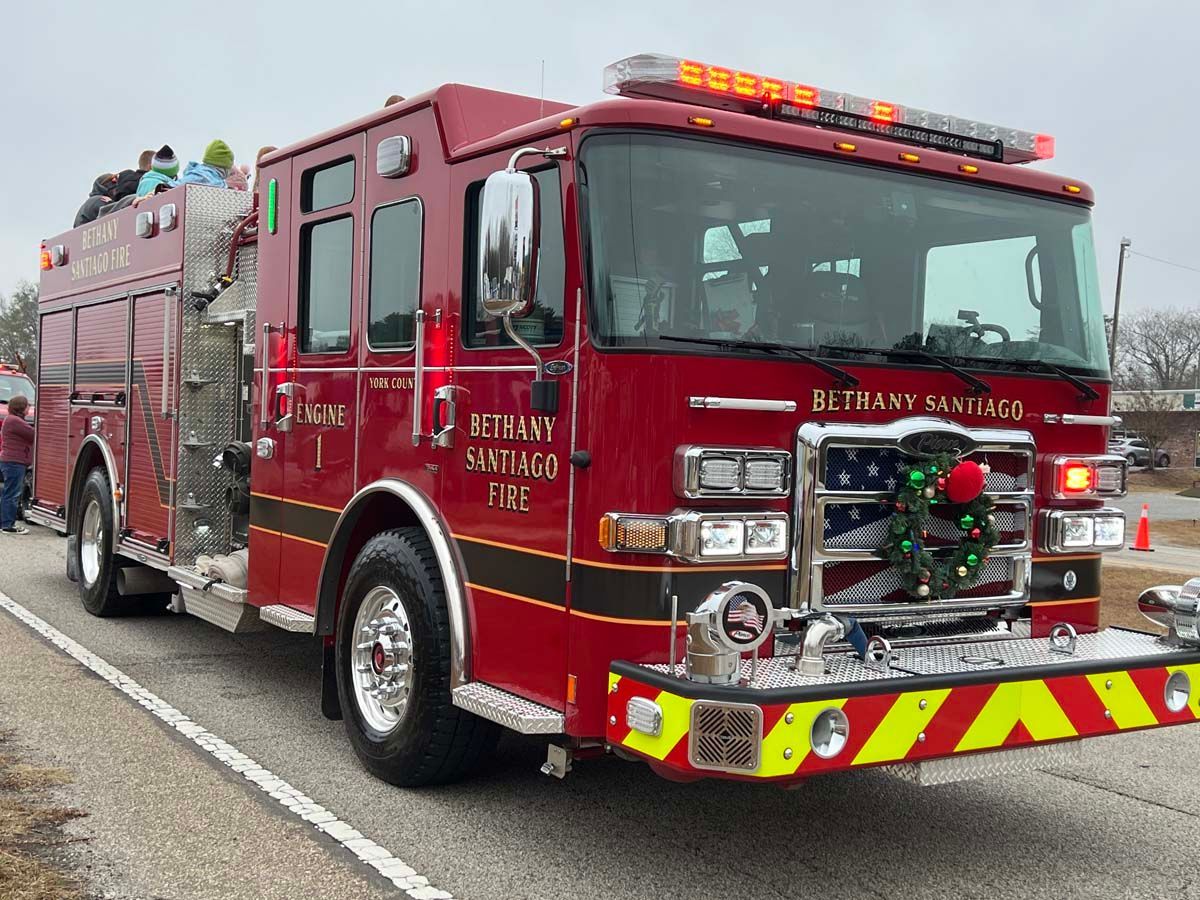 Red fire truck with holiday wreath on front parked on a roadside, crew visible on top