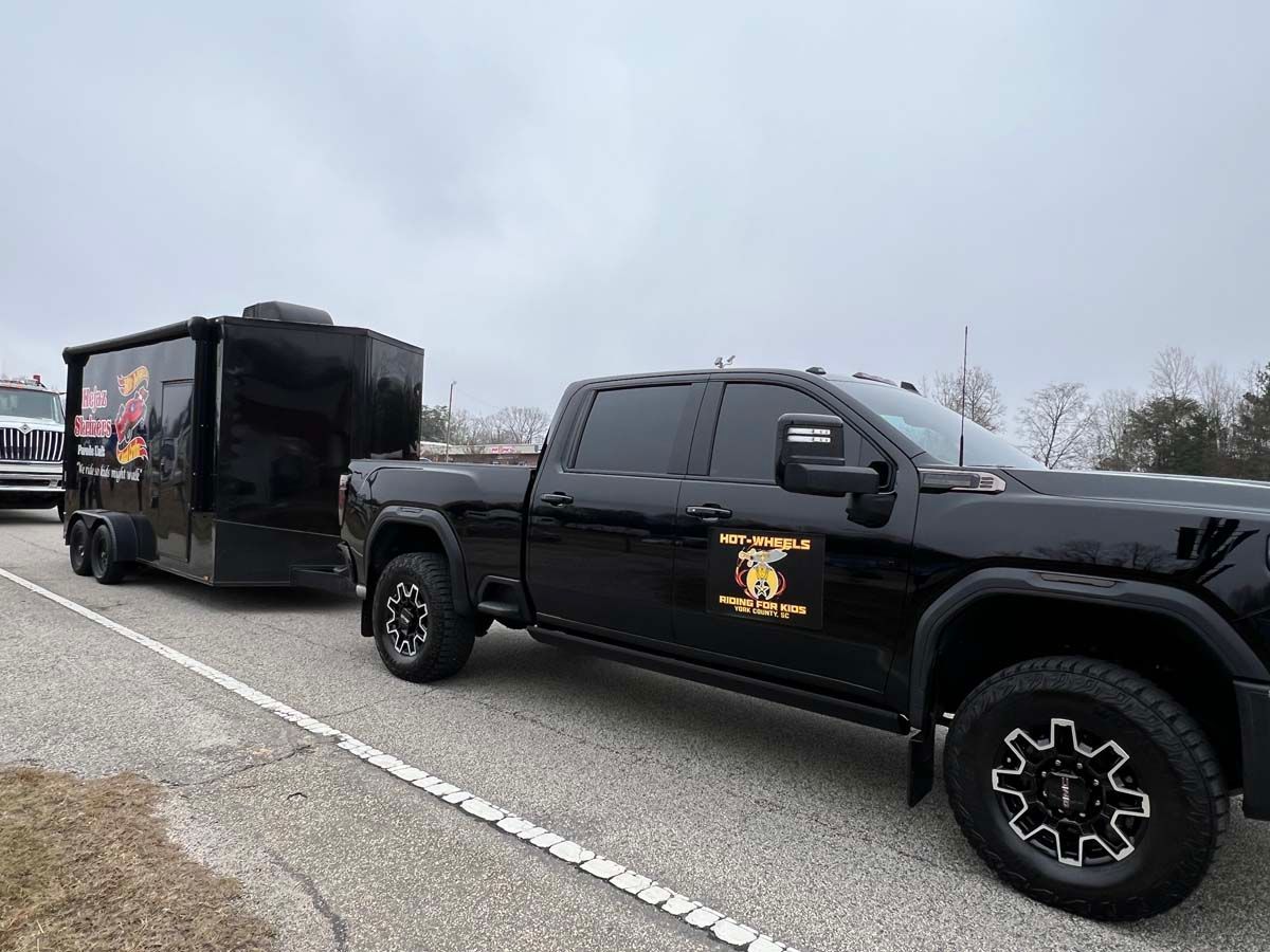 Black pickup truck towing a black enclosed trailer on a highway under cloudy skies
