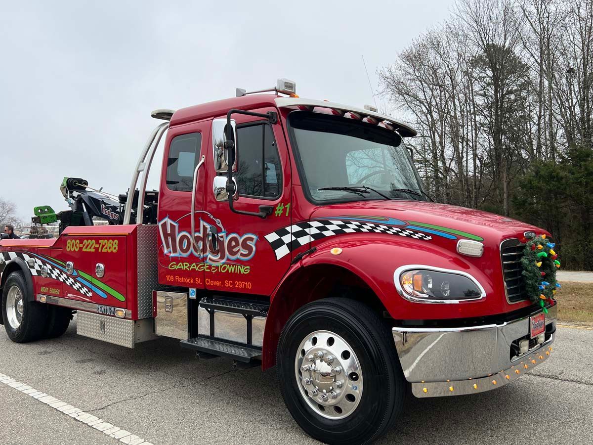 Red tow truck with “Hobbs” logo parked on a road beside leafless trees.