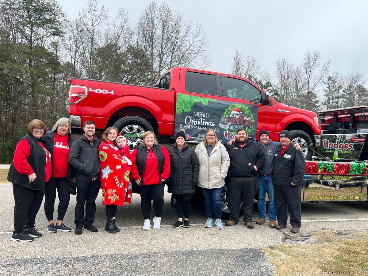 Group posing beside a red truck with holiday-themed decorations and signage outdoors.