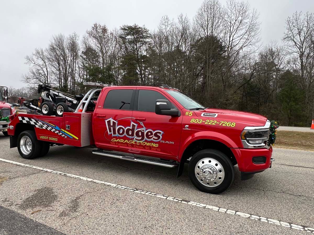 Red Hodges tow truck parked on a road with a car on its flatbed, wooded background