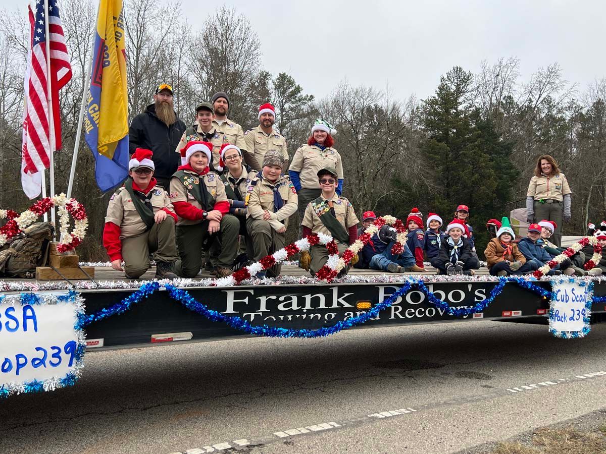 People posing on a decorated parade float with flags and a banner reading “Frank Ross Recovery”