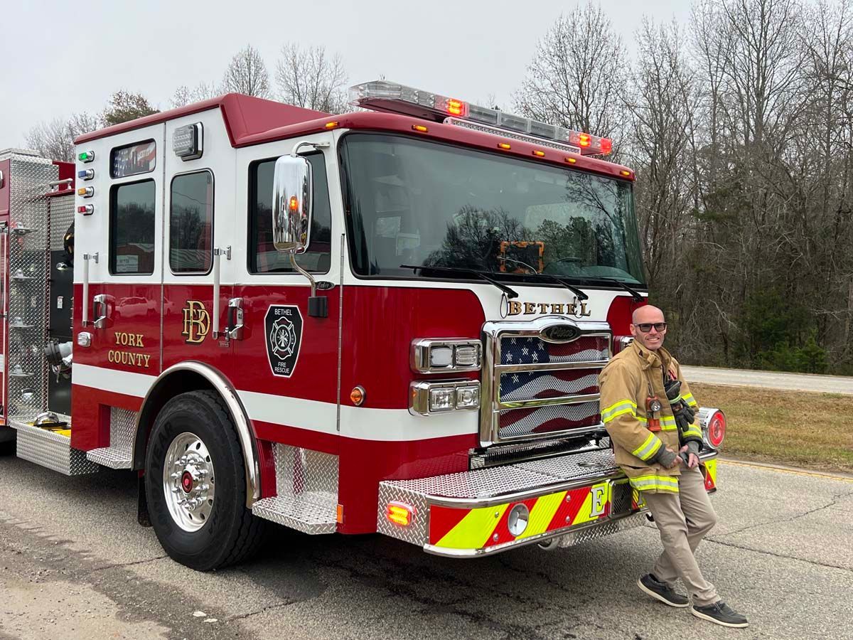 Fire truck parked on road with a firefighter in yellow gear standing beside it