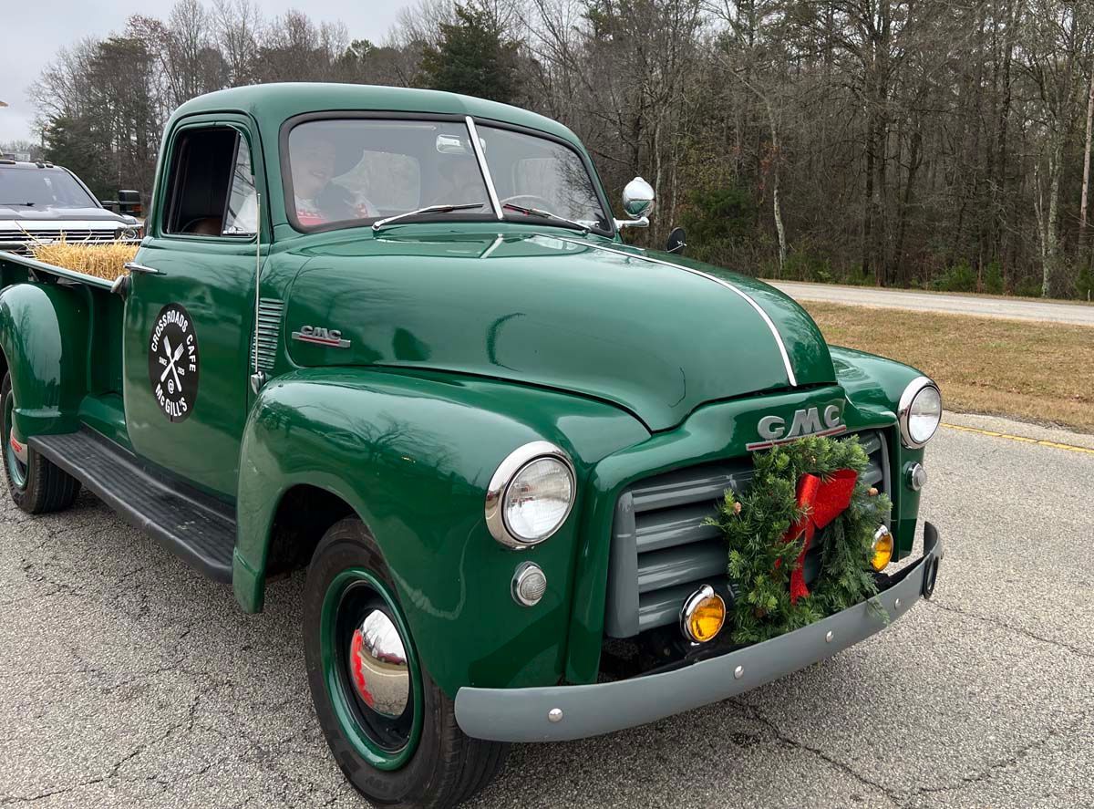 Vintage green pickup truck decorated with a holiday wreath, parked on a roadside