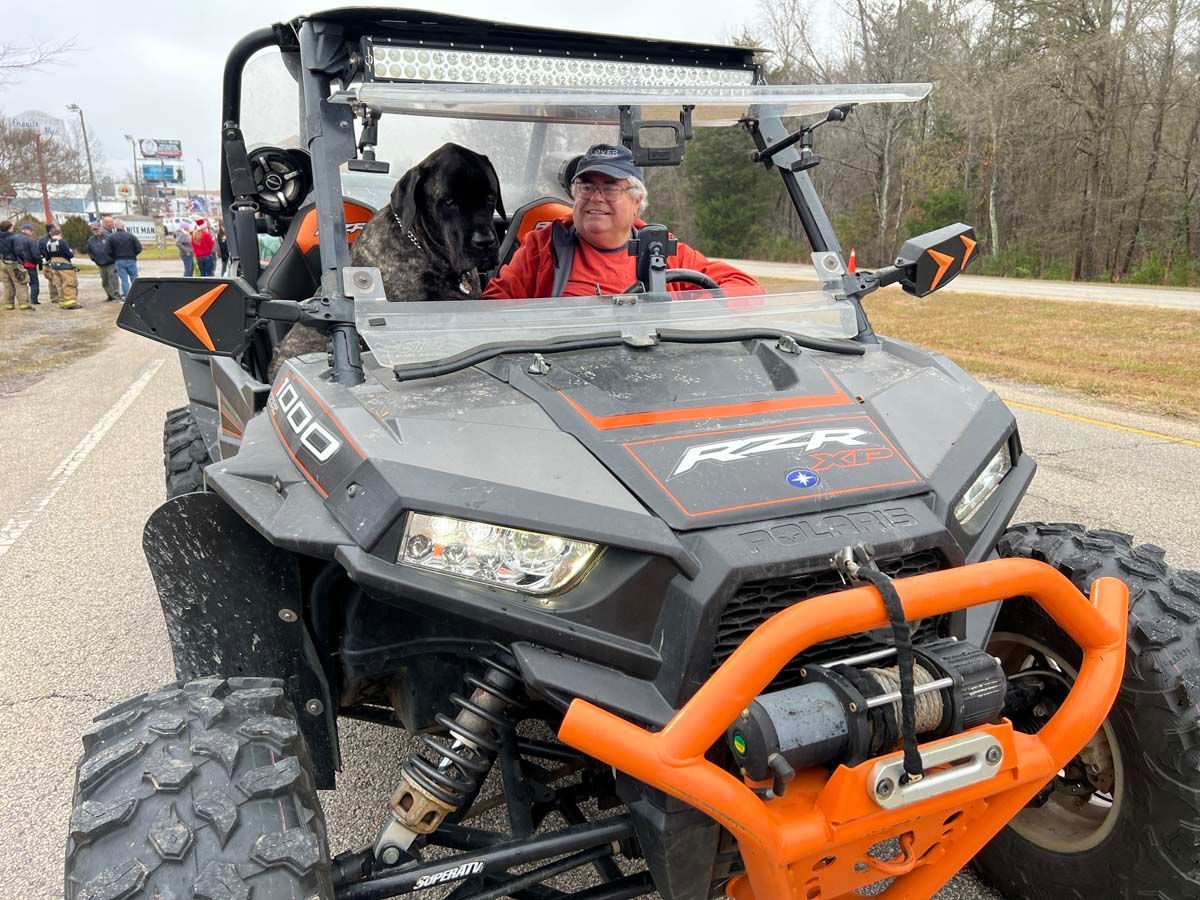 Two people riding in a black and orange off-road vehicle on a road with trees nearby