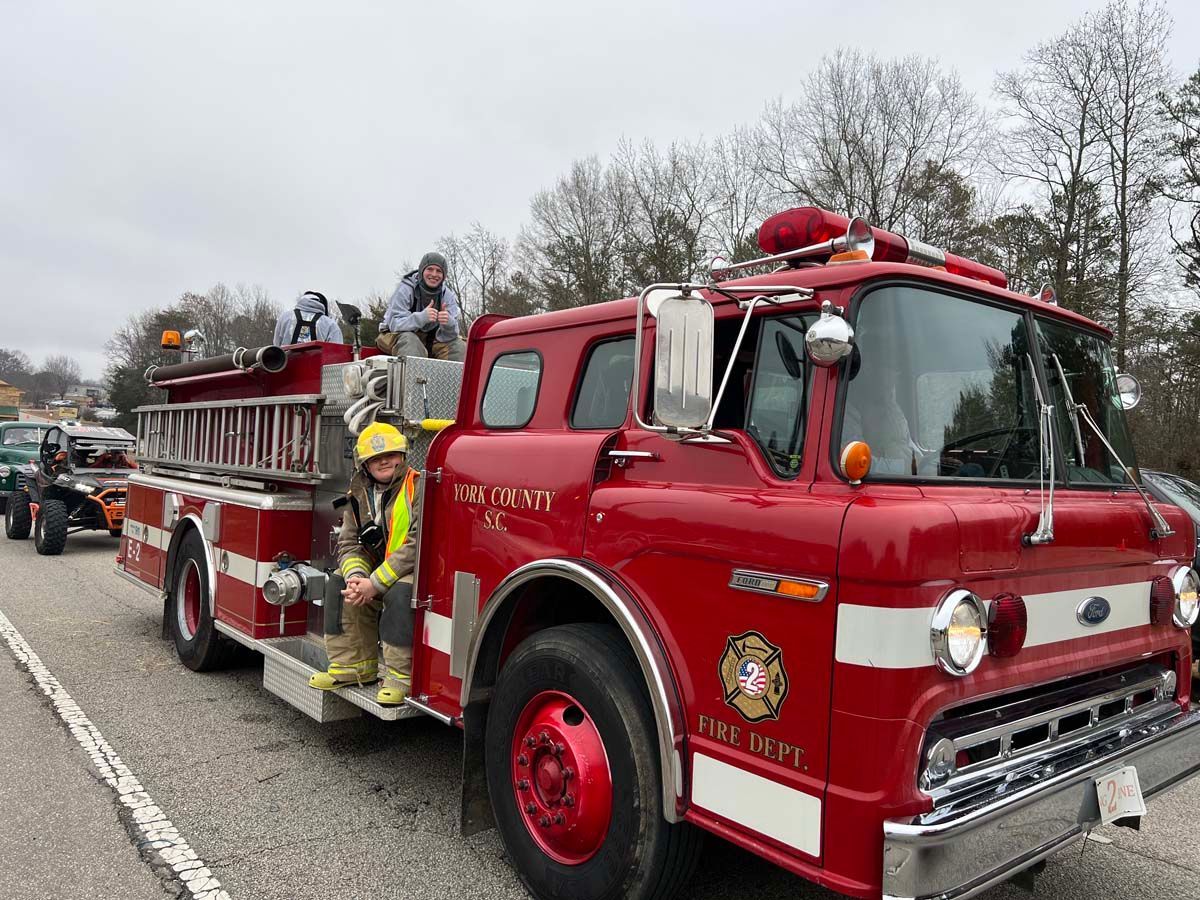 Red fire truck with firefighters parked on a wet roadside under gray winter trees