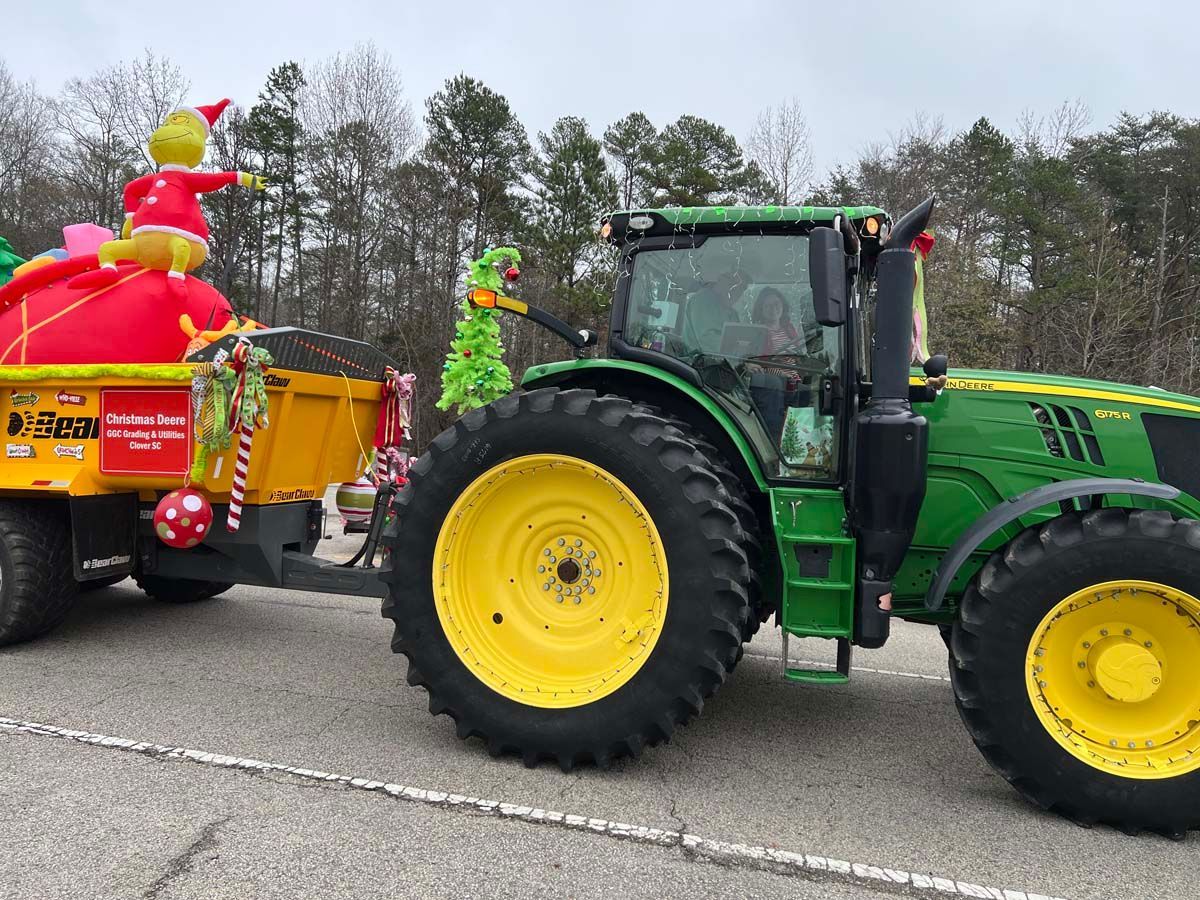 Green tractor towing yellow wagon with red decorations on a road, with trees in the background