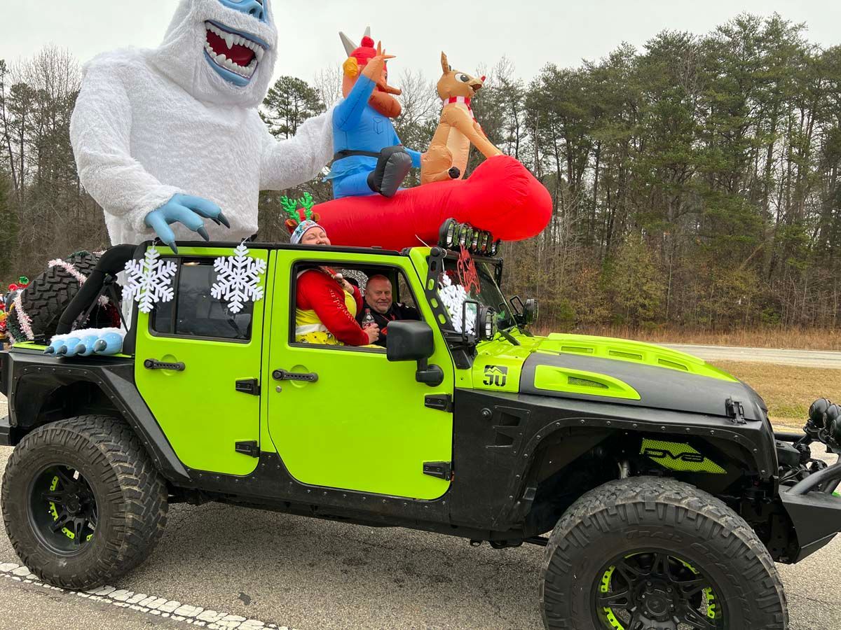 Bright green off-road Jeep with costumed characters riding on top in a wooded outdoor setting