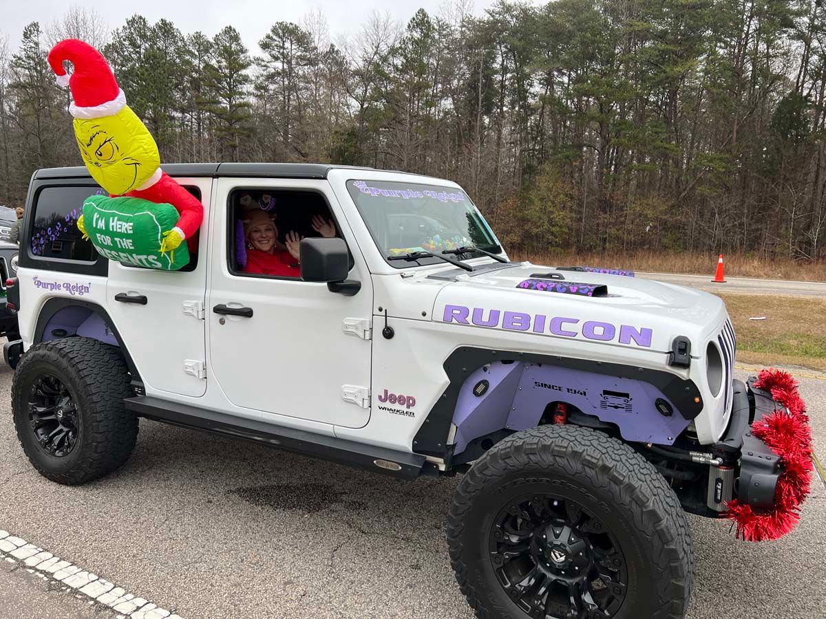 White Jeep Rubicon with colorful holiday decorations driving on a road, driver visible inside