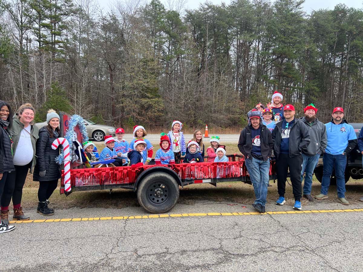 Group of people posing beside a red wagon decorated for a holiday parade in a wooded roadside setting