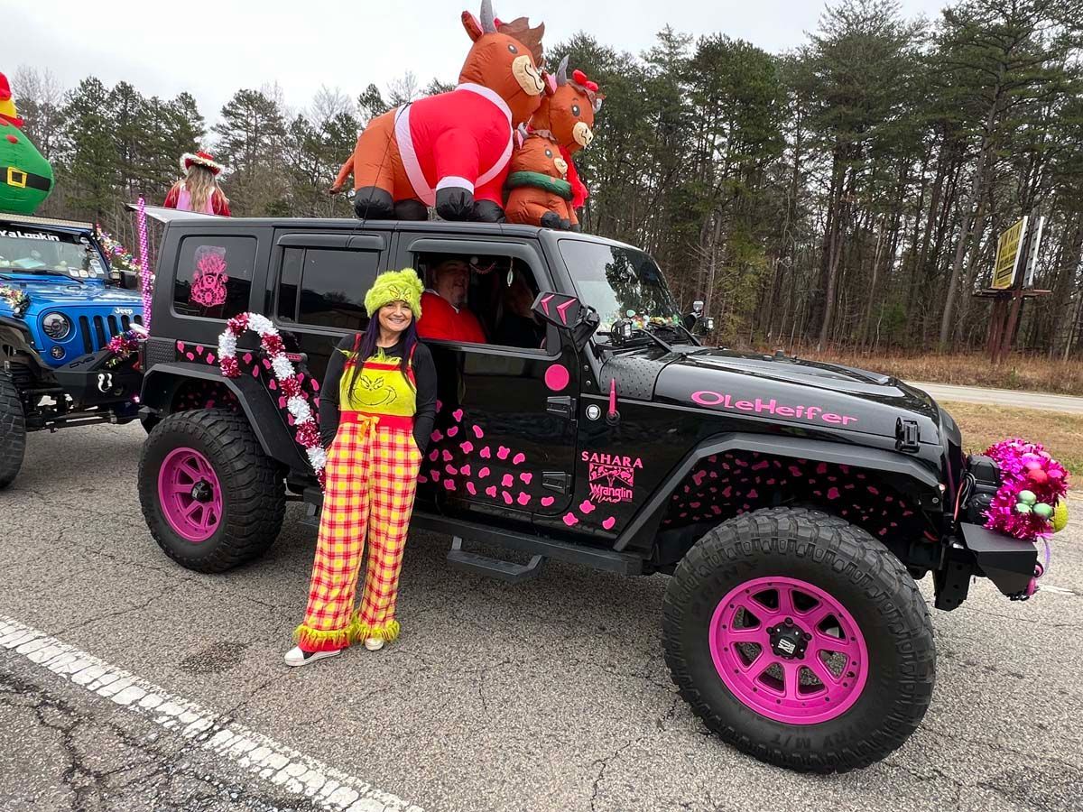 Person in colorful outfit posing beside a black Jeep with pink accents and a large Santa decoration on top