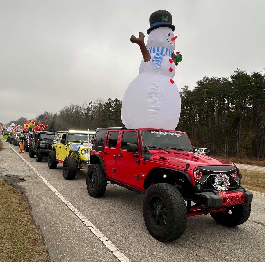 Jeep parade with a red Wrangler leading, featuring a giant inflatable snowman on a truck.