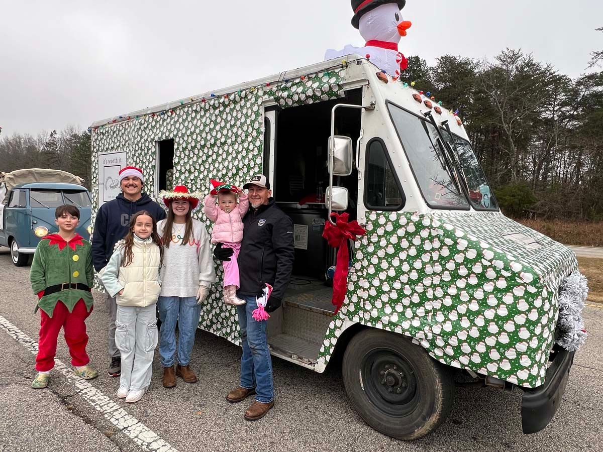People posing beside a festive truck wrapped in green-and-red holiday paper with Santa on top