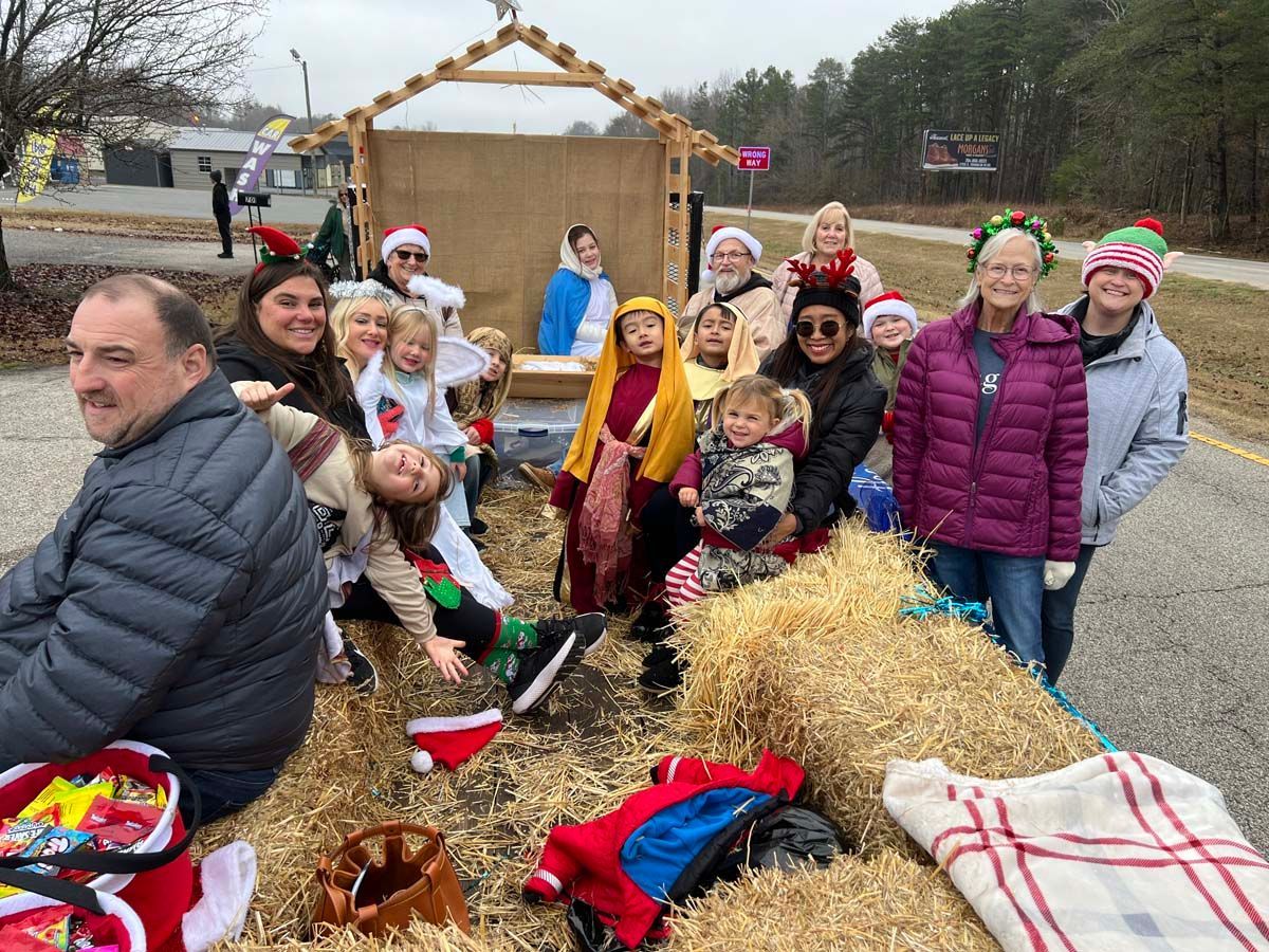 Group gathered outdoors beside straw bales and festive decorations, posing for a photo on a cloudy day
