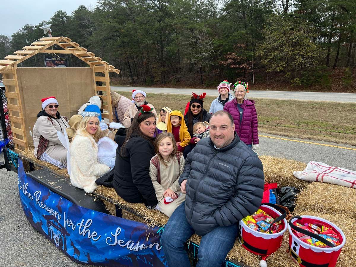 People on a decorated parade float with baskets of gifts in a grassy roadside setting