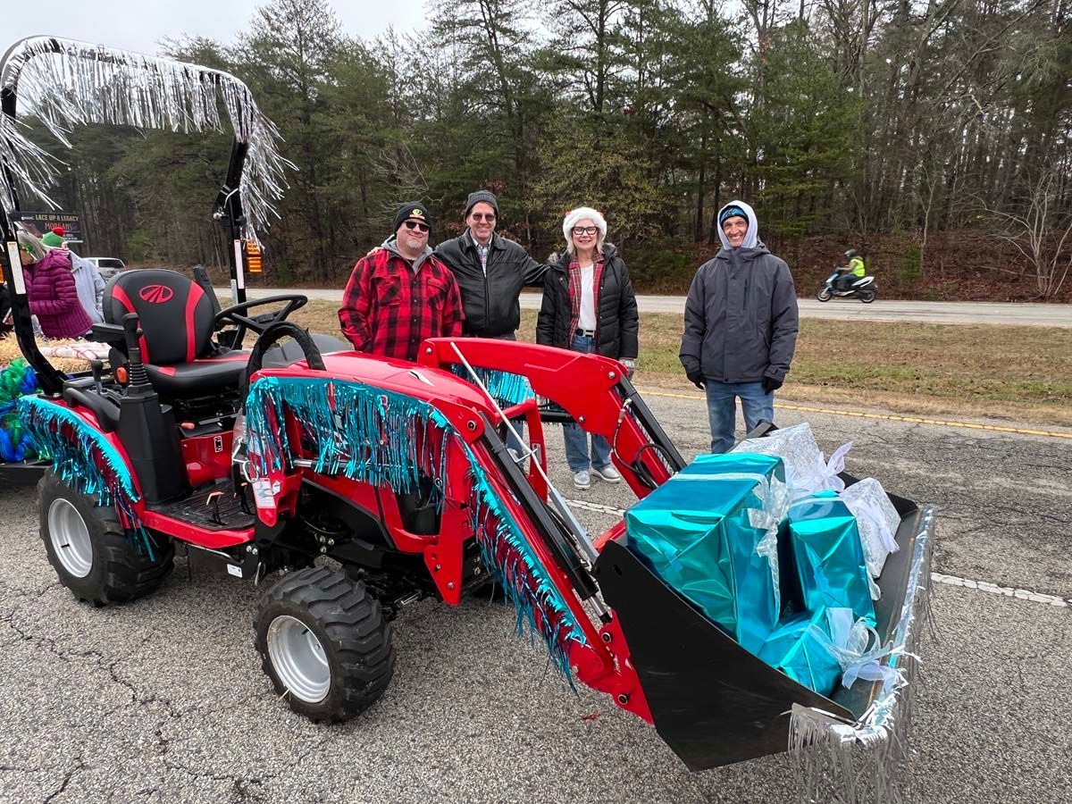 Red tractor with front loader and gift-wrapped bundle, with four people standing behind it outdoors.