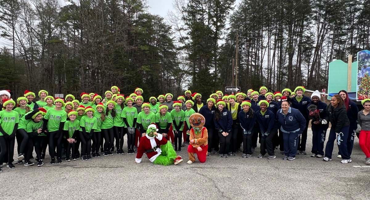 Large group in neon hats posing outdoors in a wooded area, with two people kneeling in front.