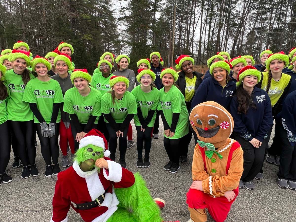 Group in neon green shirts and hats posing outdoors, with two festive characters in front.