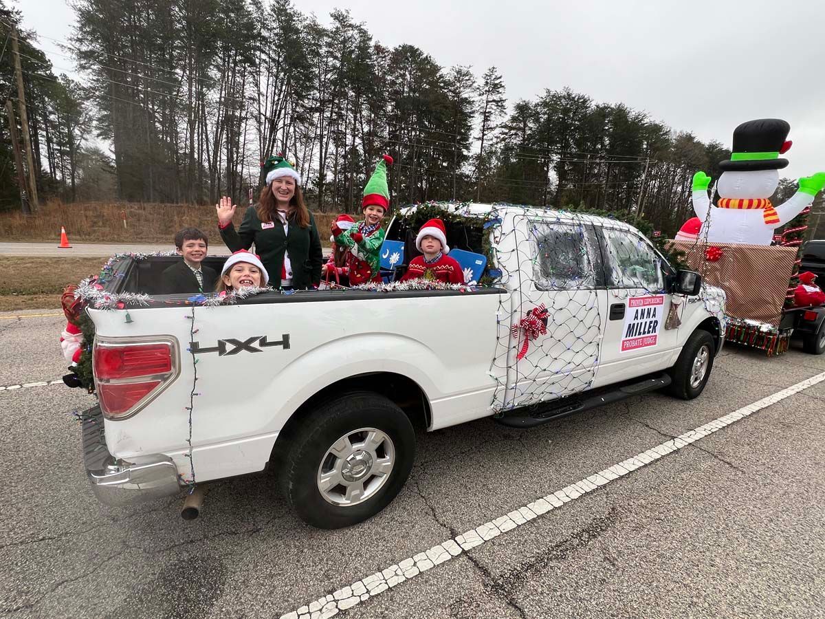 White pickup truck carrying people in Santa hats during a holiday parade on a road