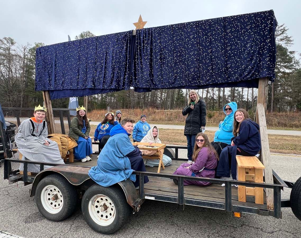 People seated on a decorated parade float with blue drapes and a gold star, outdoors on a cloudy day.