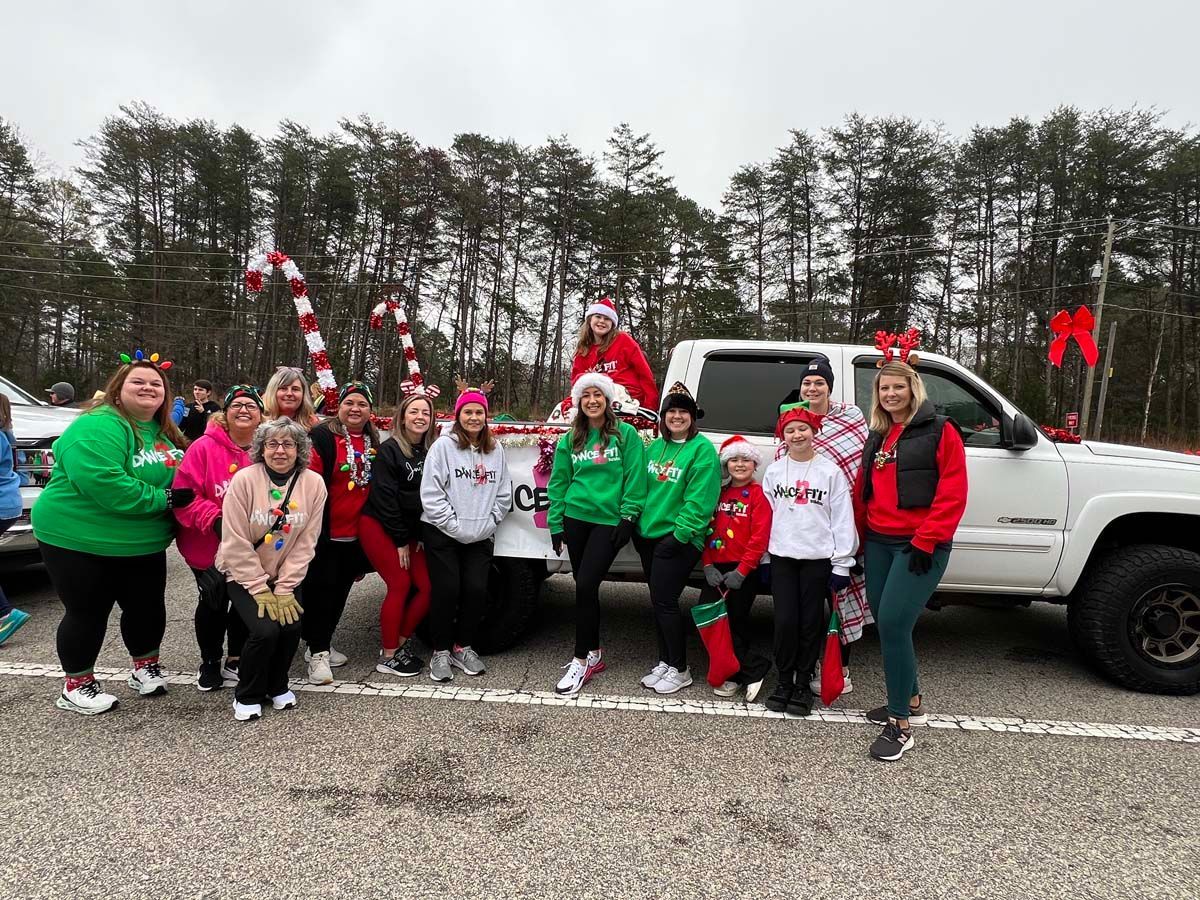 Group of people in Christmas sweaters posing beside a white pickup truck on a roadside outdoors