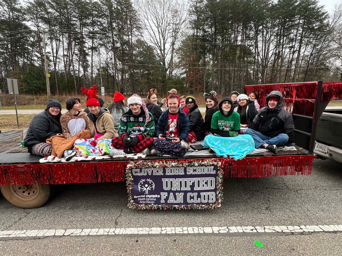Group posing on a red parade trailer with toys and a “U Pickle Fan Club” sign in a winter setting