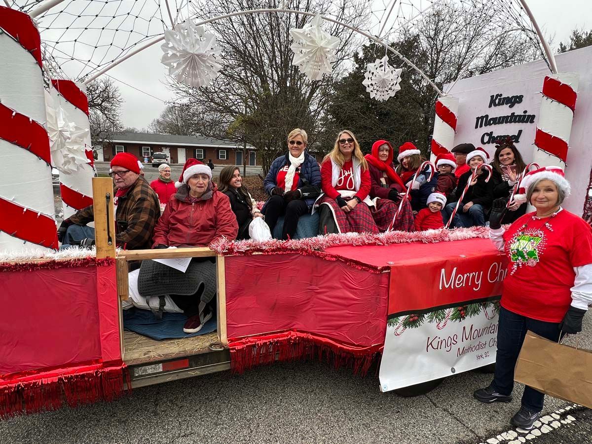 People in red and white Christmas parade float waving with “Merry Christmas” banner