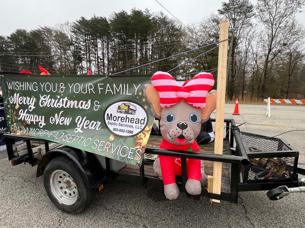 Holiday parade float with Merry Christmas and Happy New Year signs, teddy bear decoration, and “Morehead” logo