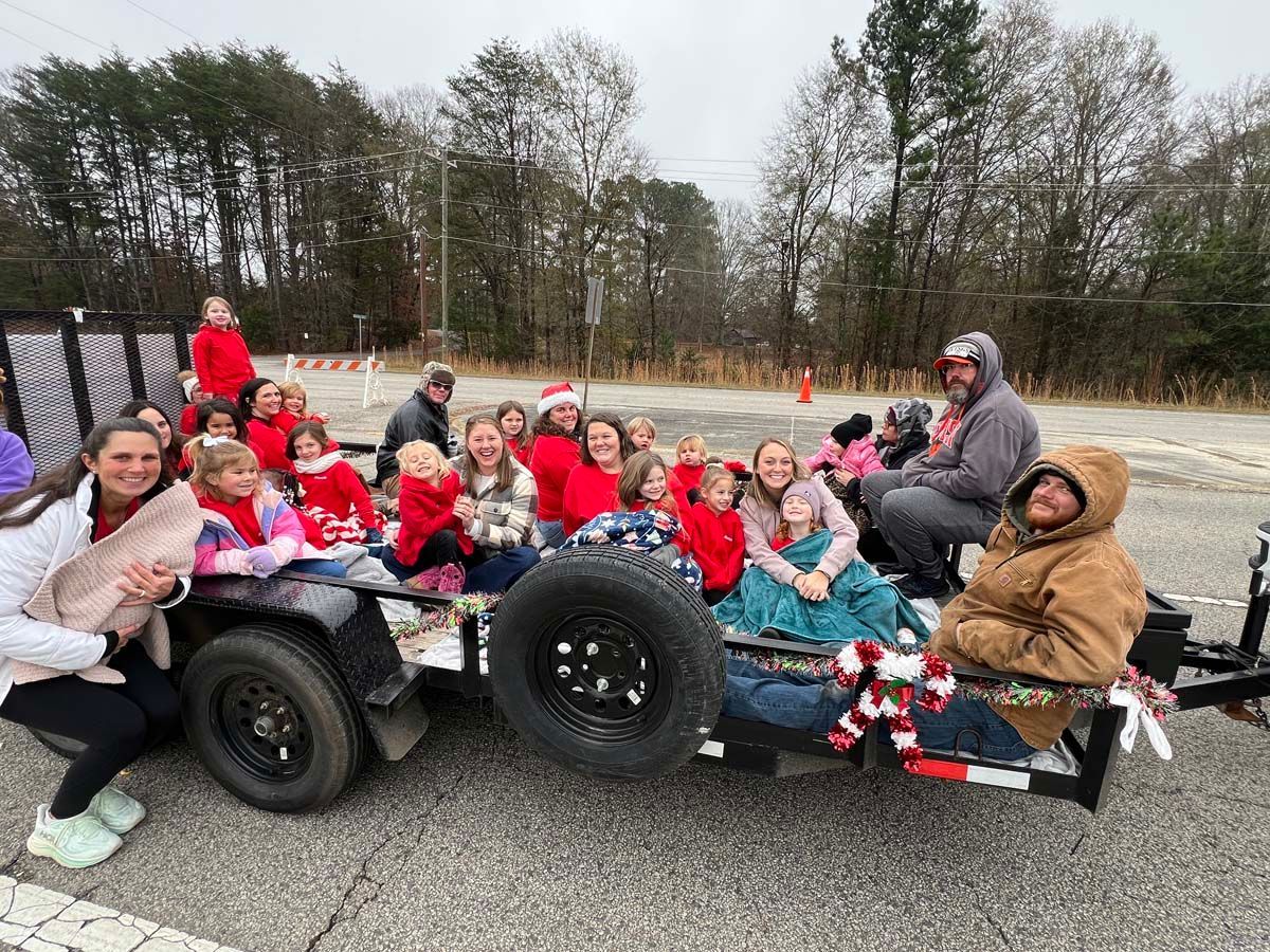 Group in red and gray jackets seated on a trailer outdoors in a wooded area