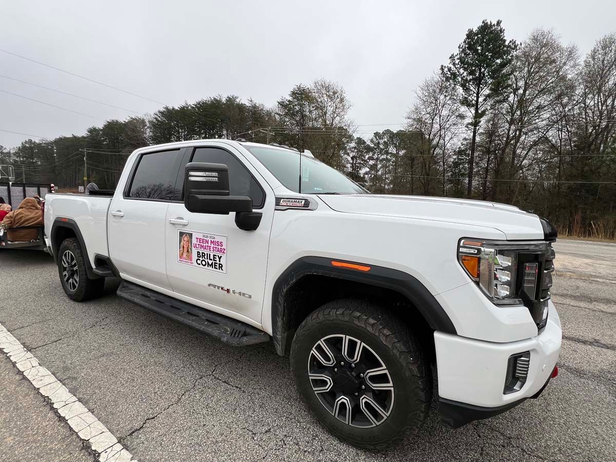 White pickup truck with a company logo parked on a roadside under overcast skies