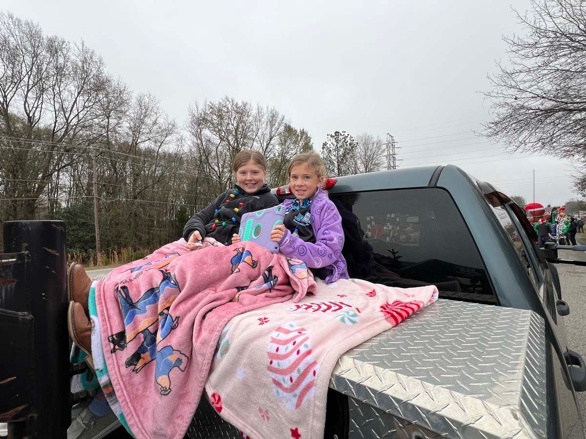 Two children sitting on a pickup truck bed covered with pink blankets outdoors