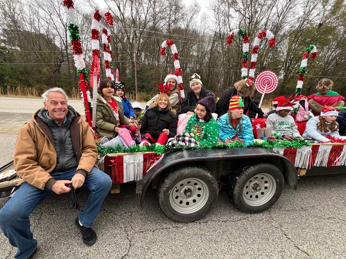 People on a decorated parade float with candy cane poles and red-white-green holiday decorations
