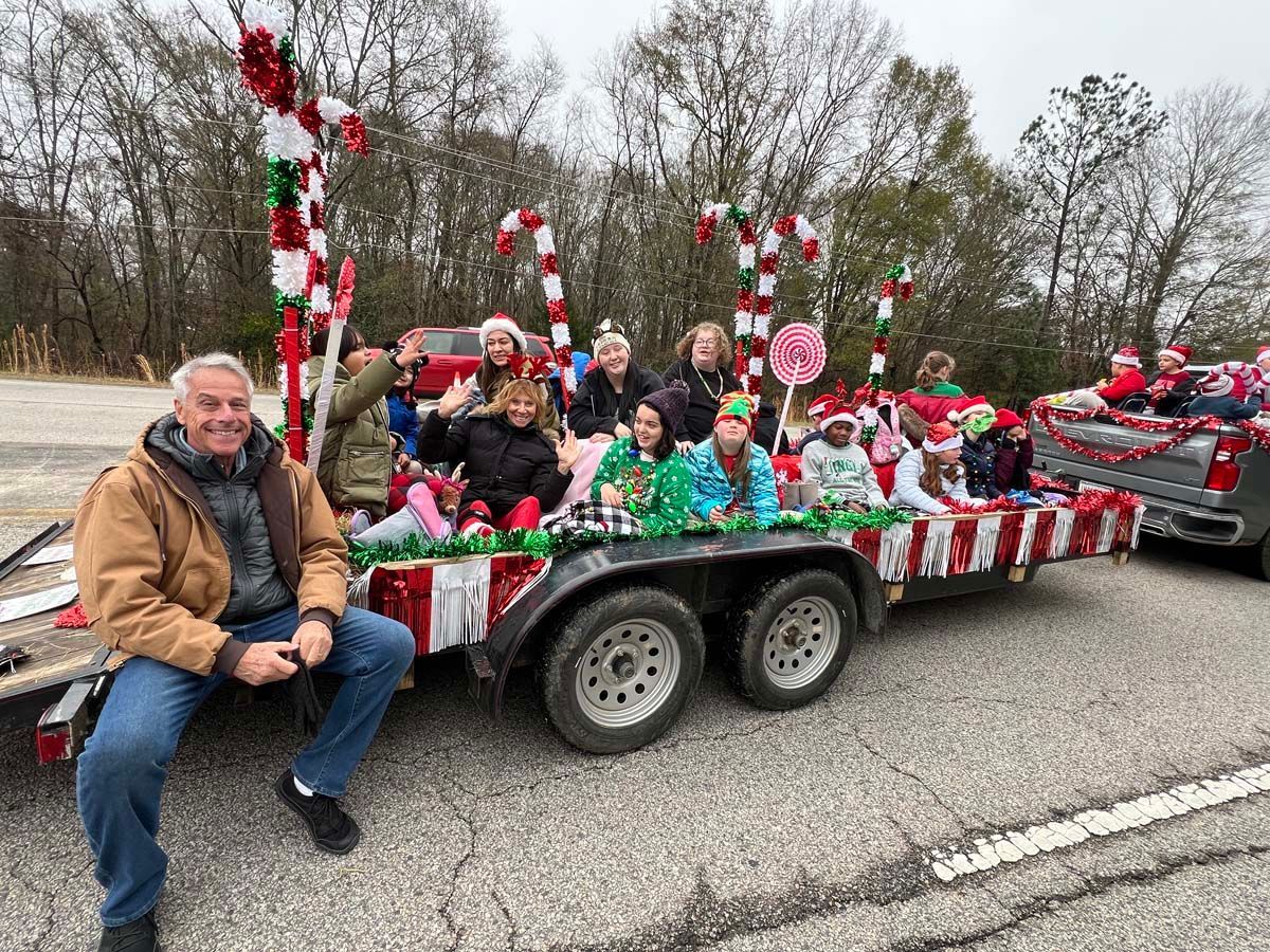 Holiday parade float with people in festive red-and-white decorations being towed beside a road