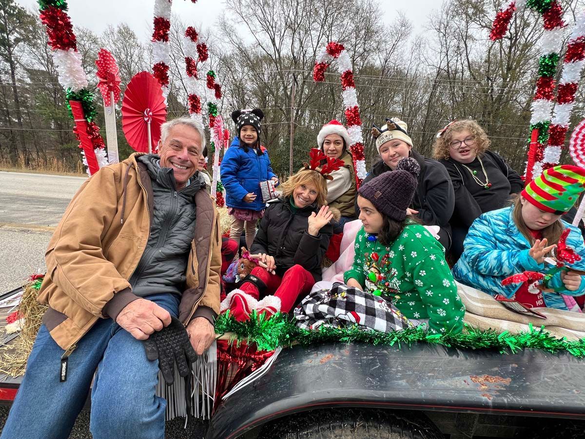 People posing on a decorated car with holiday greenery and red-and-green ornaments outdoors