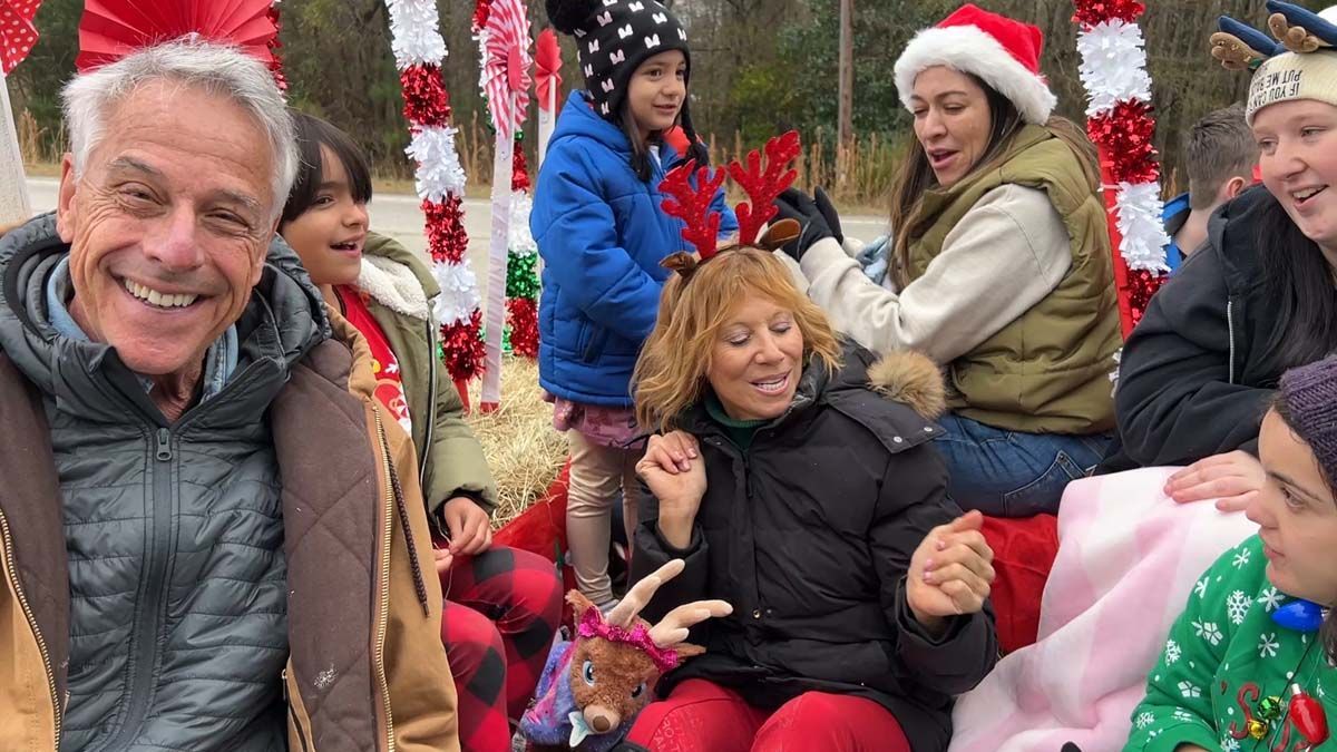 People gathered outdoors in winter clothing, smiling and posing with holiday decorations.
